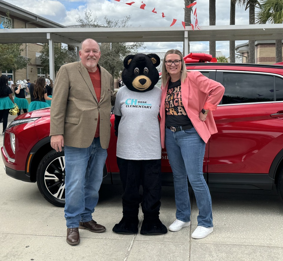 Daytona Mitsubishi and Daytona Kia Sales Manager Tom Gross, the Champion mascot, and the Volusia County Schools 2025 Teacher of the Year Emily Fagerstrom.